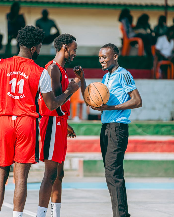 A basketball coach encourages two players during a friendly practice game outdoors.