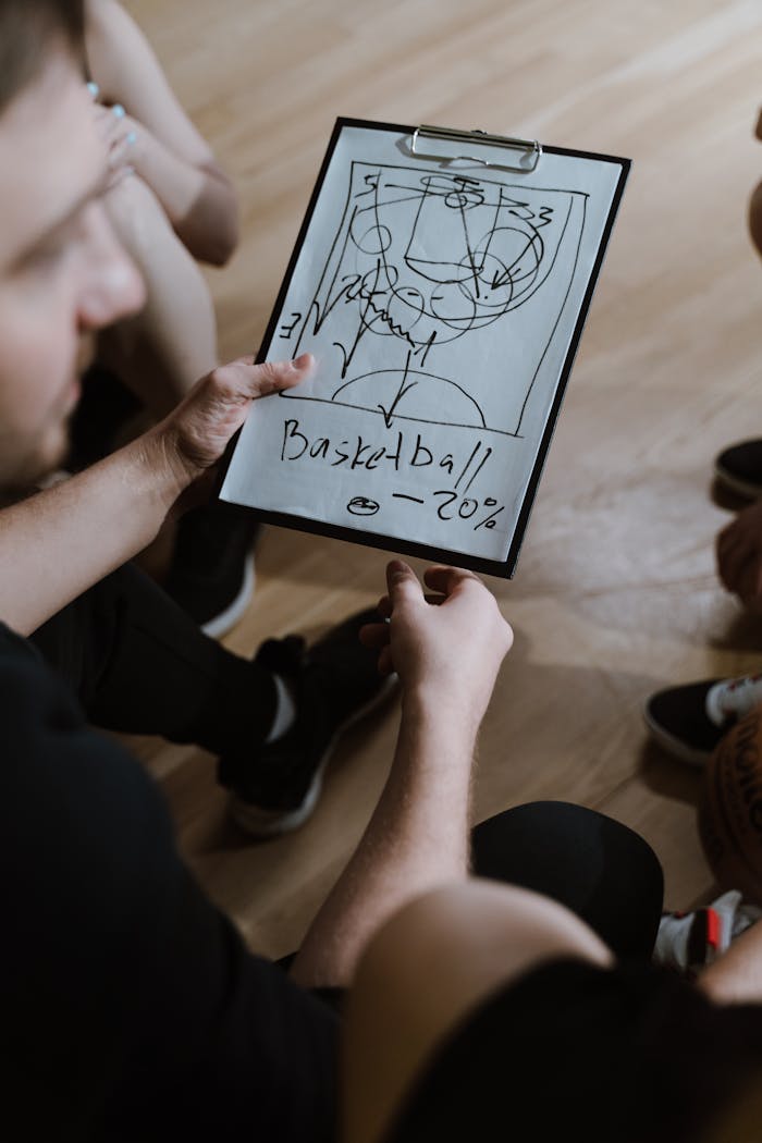 Coach presents a basketball strategy on clipboard during indoor team huddle.
