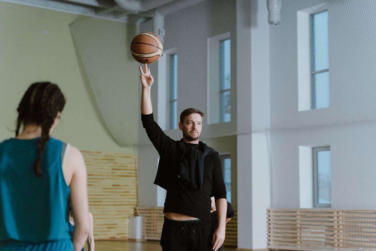 Coach spinning a basketball indoors, guiding a young player during a gym practice session.